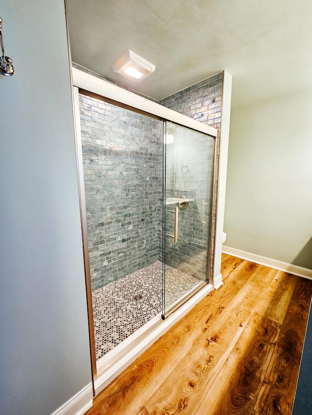 bathroom featuring a stall shower, toilet, baseboards, and wood finished floors