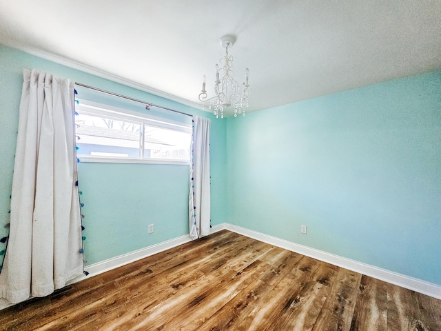 spare room featuring a notable chandelier, baseboards, and wood finished floors