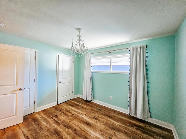 unfurnished bedroom with baseboards, an inviting chandelier, and wood finished floors