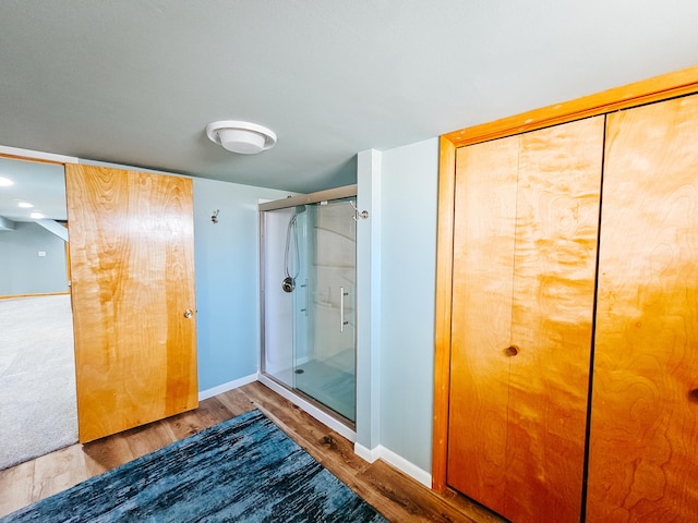 bathroom featuring baseboards, wood finished floors, and a shower stall