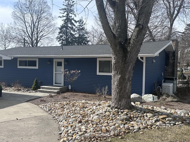 single story home with central air condition unit, a chimney, and a shingled roof