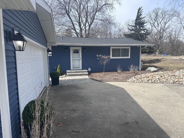 exterior space with concrete driveway, a garage, and a shingled roof