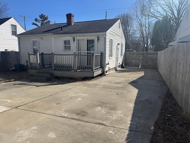 rear view of house featuring a deck, a patio, fence, and a chimney