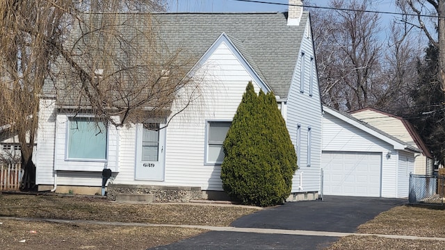 view of front of home with driveway, roof with shingles, an outdoor structure, a garage, and a chimney