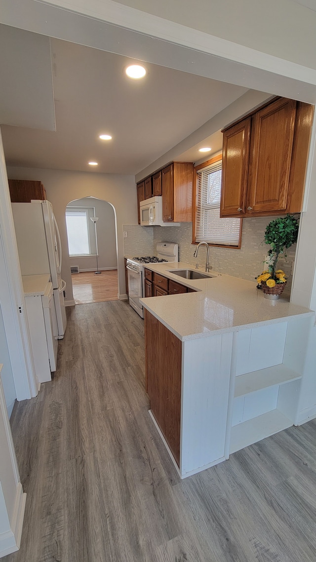 kitchen featuring a sink, white appliances, arched walkways, and wood finished floors