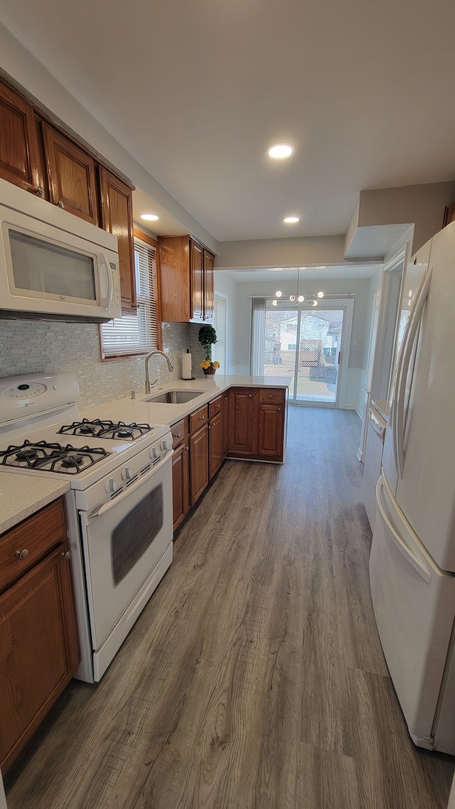 kitchen with dark wood finished floors, light countertops, a peninsula, white appliances, and a sink