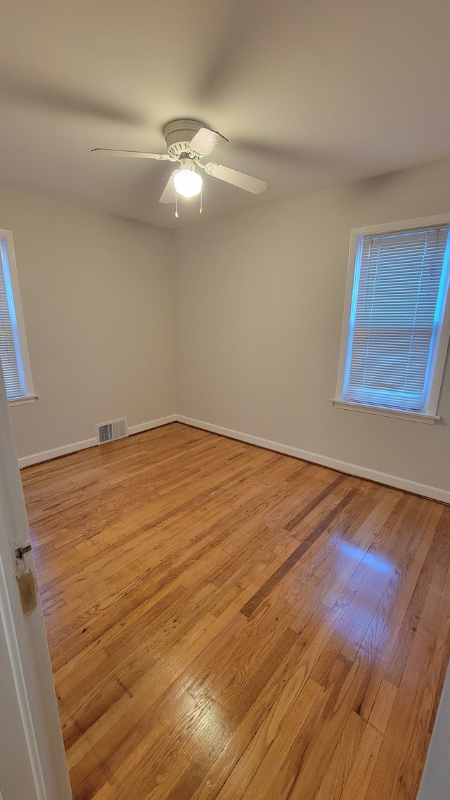 empty room featuring light wood finished floors, visible vents, ceiling fan, and baseboards