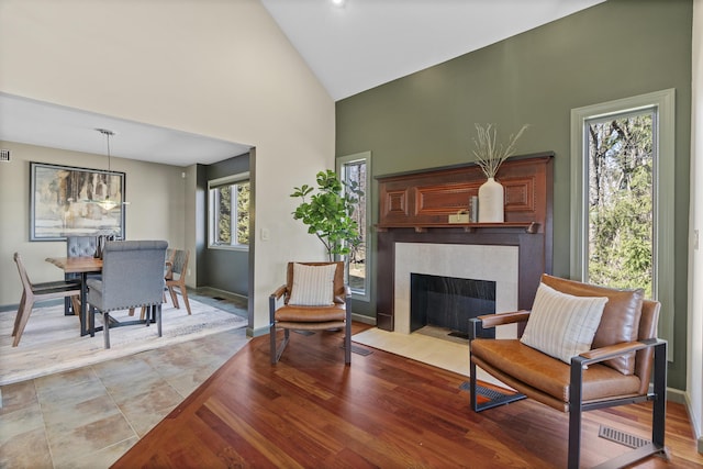 living area with a fireplace, a healthy amount of sunlight, baseboards, and high vaulted ceiling