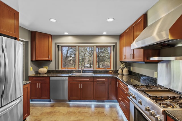 kitchen with dark stone countertops, appliances with stainless steel finishes, wall chimney exhaust hood, and a sink