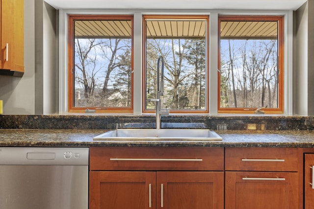 kitchen with dishwasher, dark stone countertops, brown cabinetry, and a sink