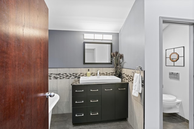 full bath with toilet, a freestanding bath, vanity, tile patterned floors, and tile walls