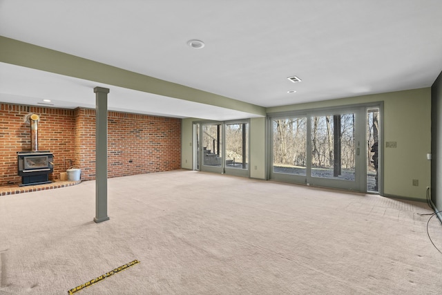 unfurnished living room featuring visible vents, carpet, brick wall, baseboards, and a wood stove