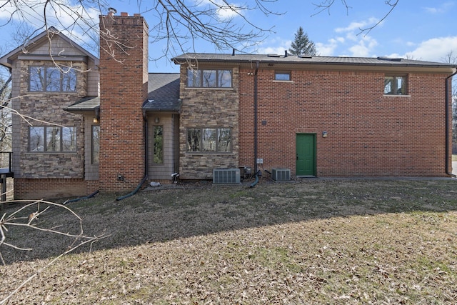 back of property featuring cooling unit, stone siding, and a yard