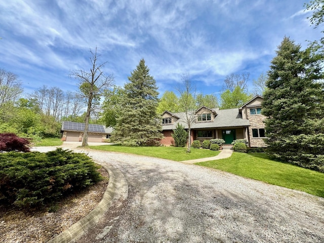 5557 N Territorial Rd, Ann Arbor, MI 48105 - view of front of property with stone siding, curved driveway, a front yard, and solar panels