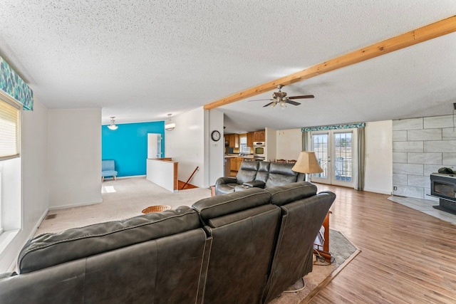 living room with wood finished floors, a ceiling fan, a wood stove, vaulted ceiling with beams, and a textured ceiling