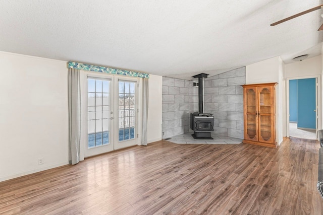 unfurnished living room with a textured ceiling, wood finished floors, baseboards, ceiling fan, and a wood stove