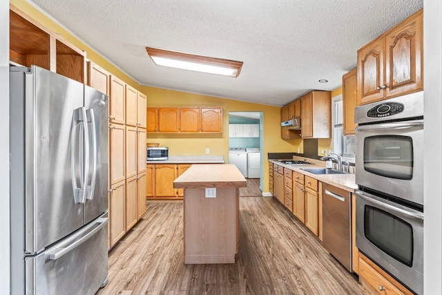 kitchen with washing machine and clothes dryer, light countertops, vaulted ceiling, light wood-style floors, and stainless steel appliances