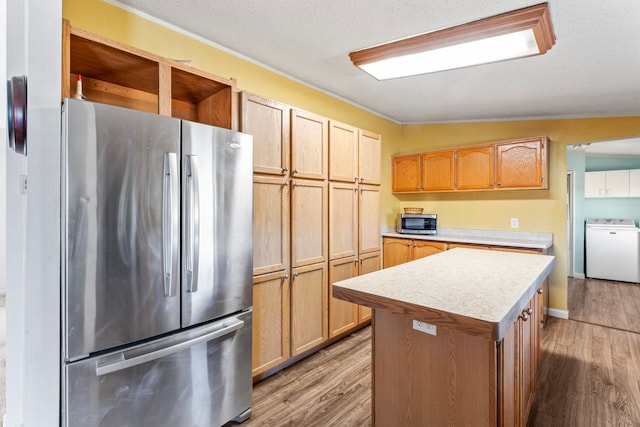 kitchen with appliances with stainless steel finishes, washer / clothes dryer, light countertops, and wood finished floors