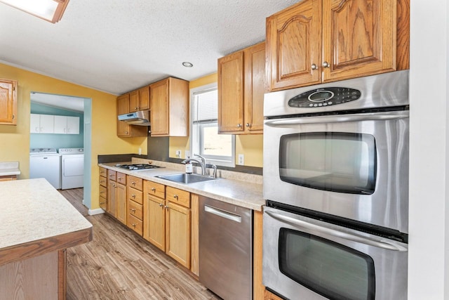 kitchen featuring light wood-style flooring, under cabinet range hood, a sink, washing machine and dryer, and stainless steel appliances