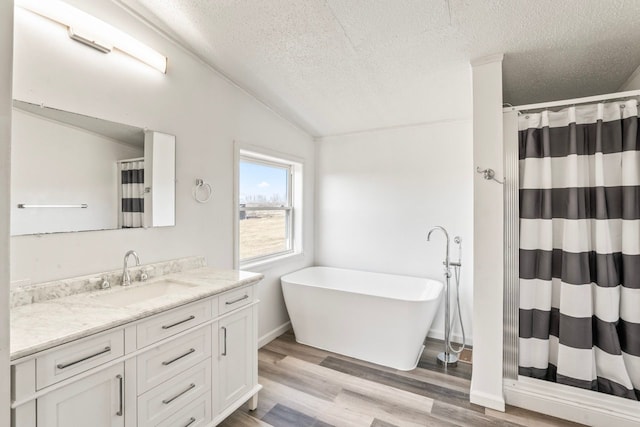 full bath featuring a textured ceiling, wood finished floors, a soaking tub, vanity, and vaulted ceiling