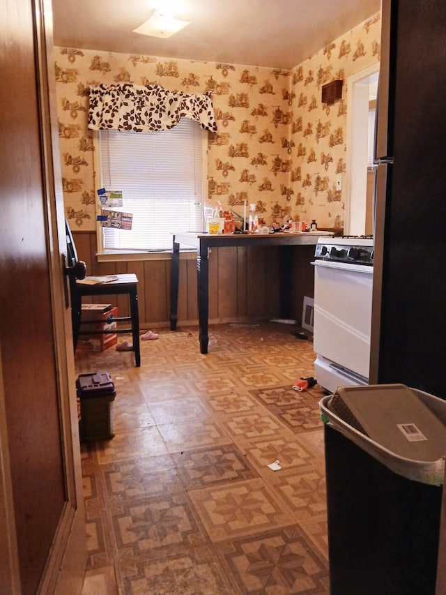 kitchen with white gas range, light floors, wallpapered walls, and freestanding refrigerator