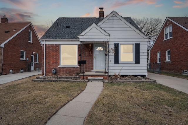 bungalow with driveway, roof with shingles, a chimney, a front lawn, and brick siding