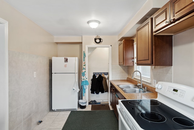 kitchen with white appliances, light tile patterned floors, brown cabinetry, a sink, and tile walls