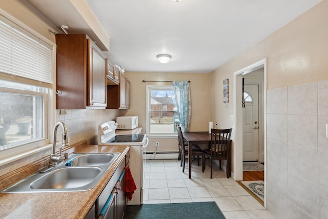 kitchen with a sink, white appliances, light countertops, light tile patterned floors, and baseboard heating