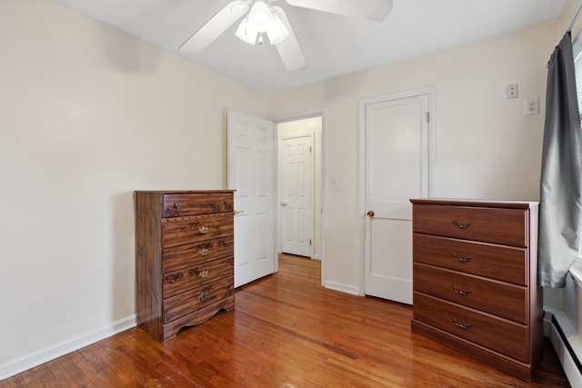 bedroom with baseboard heating, ceiling fan, baseboards, and wood-type flooring