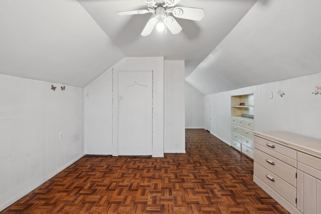 additional living space featuring built in shelves, wooden walls, lofted ceiling, and a ceiling fan