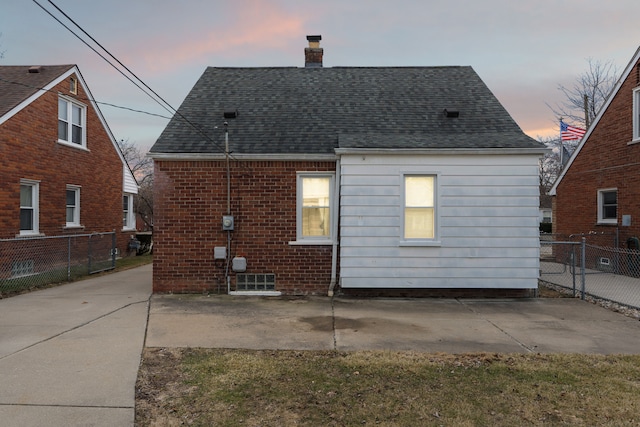 back of house at dusk featuring a shingled roof, a chimney, a patio, and fence