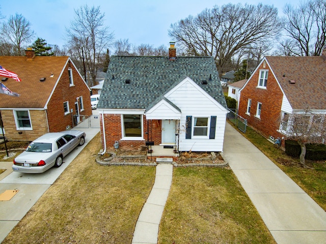 view of front facade featuring roof with shingles, driveway, a chimney, a front lawn, and brick siding