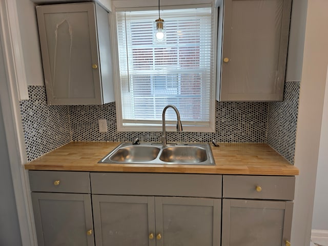 kitchen with a sink, decorative backsplash, wooden counters, and hanging light fixtures