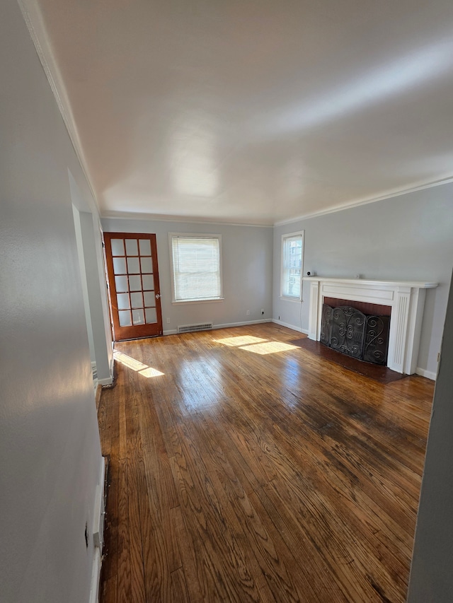 unfurnished living room featuring a baseboard heating unit, baseboards, a fireplace with flush hearth, ornamental molding, and hardwood / wood-style floors