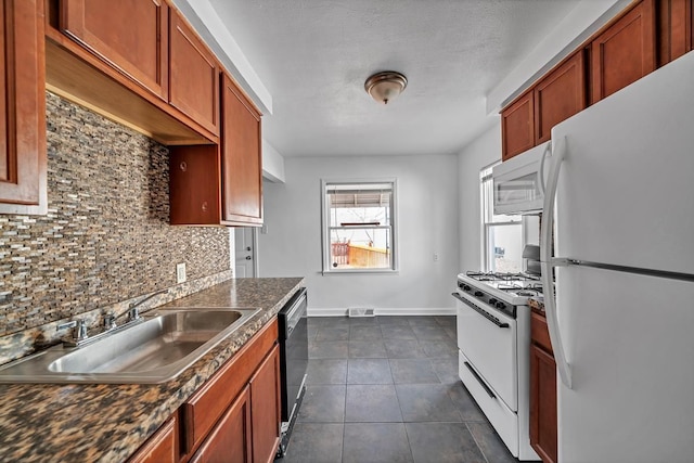 kitchen featuring white appliances, a sink, dark countertops, dark tile patterned floors, and backsplash