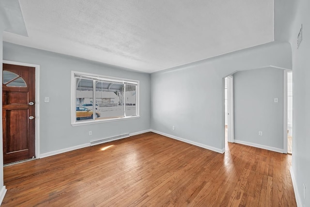 spare room with a textured ceiling, wood finished floors, baseboards, and a baseboard radiator