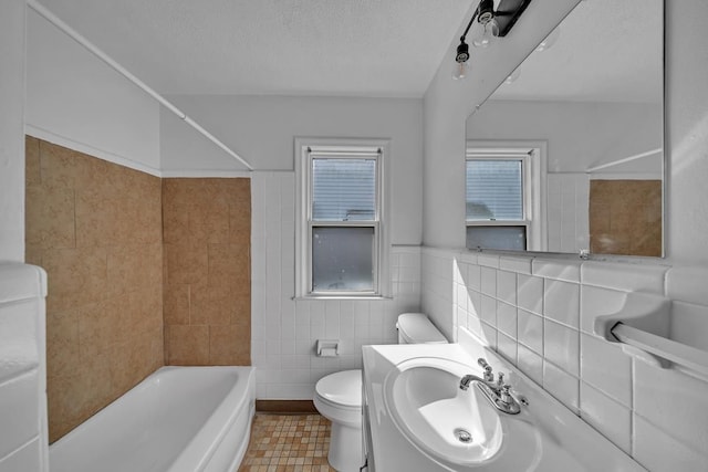 full bathroom with a sink, bathtub / shower combination, a textured ceiling, tile walls, and toilet