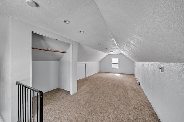 additional living space featuring carpet floors, a textured ceiling, a textured wall, and vaulted ceiling