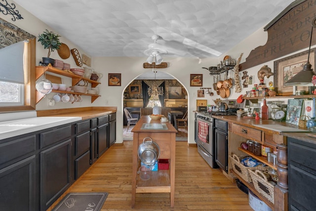 kitchen featuring open shelves, a kitchen island, gas stove, arched walkways, and light wood-style floors