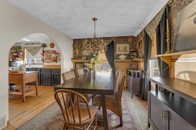 dining room featuring arched walkways, a chandelier, light wood-type flooring, and visible vents