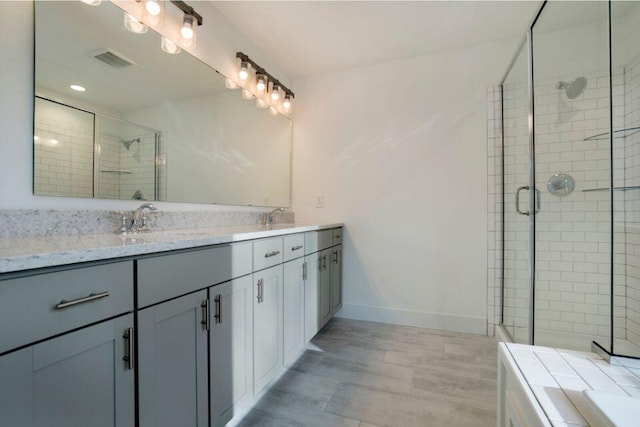 bathroom with visible vents, a shower stall, baseboards, double vanity, and a sink