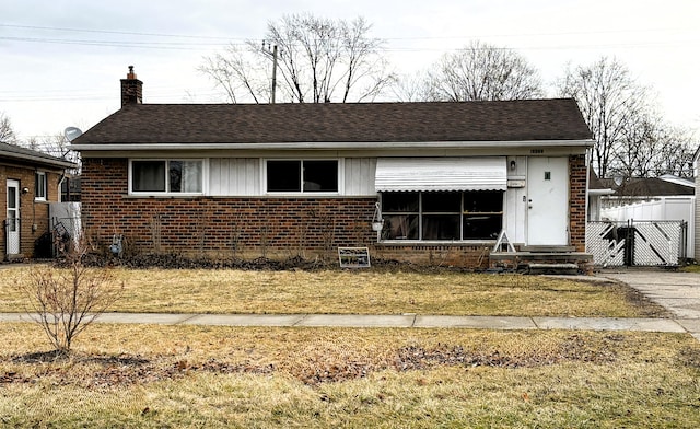 view of front of home with brick siding, fence, a front yard, roof with shingles, and a chimney