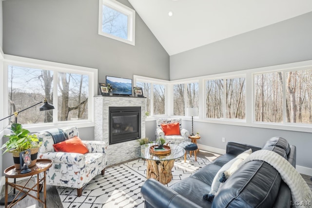 living room featuring a stone fireplace, high vaulted ceiling, and baseboards