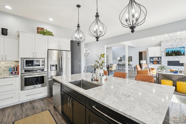 kitchen featuring an island with sink, stainless steel appliances, a notable chandelier, white cabinetry, and a sink