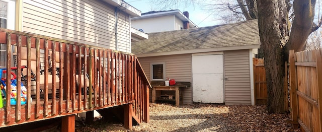 exterior space featuring a wooden deck, fence, and a shingled roof