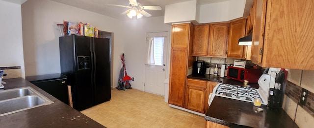 kitchen with white range with gas cooktop, brown cabinets, under cabinet range hood, black fridge with ice dispenser, and light floors