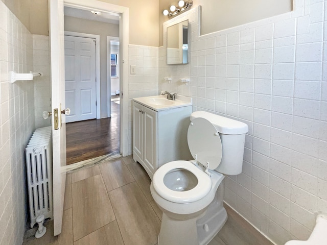 bathroom featuring radiator, wood tiled floor, toilet, vanity, and tile walls