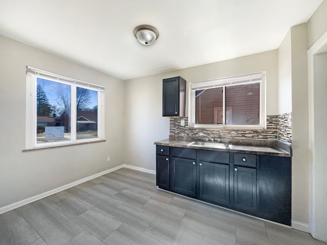 kitchen featuring decorative backsplash, dark countertops, baseboards, and a sink