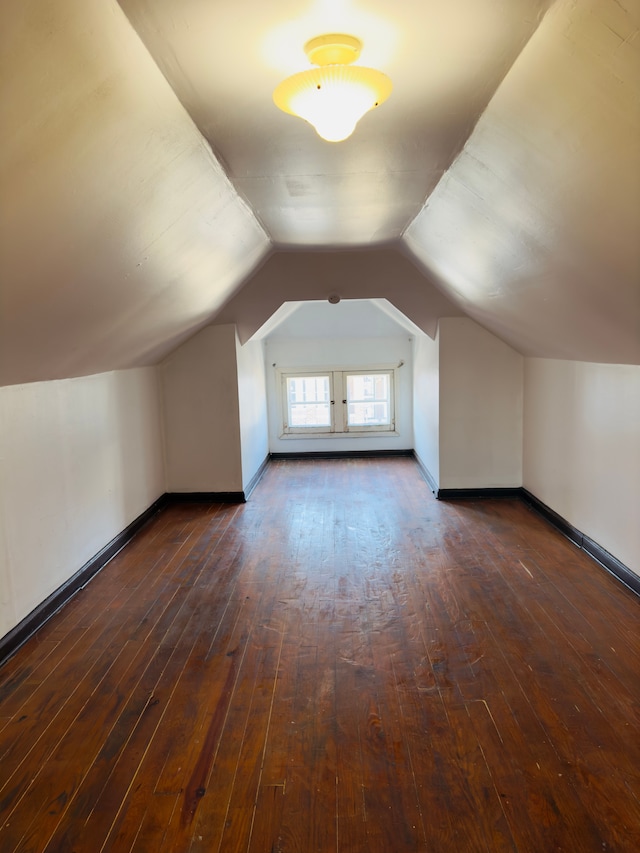 bonus room with dark wood finished floors, baseboards, and vaulted ceiling