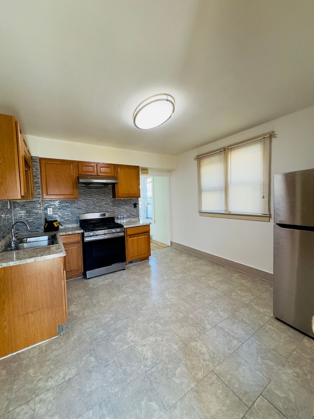 kitchen with under cabinet range hood, decorative backsplash, brown cabinets, stainless steel appliances, and a sink